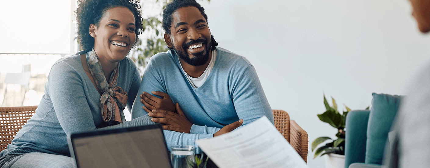 A smiling couple meets with a mortgage advisor, reviewing loan documents together in a bright, modern office setting.