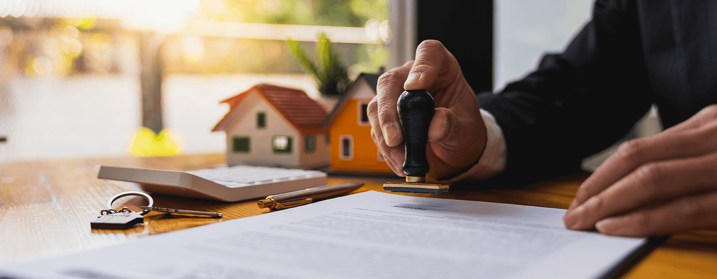 A lender stamps an employment verification letter for mortgage approval beside house models, keys, and a pen.