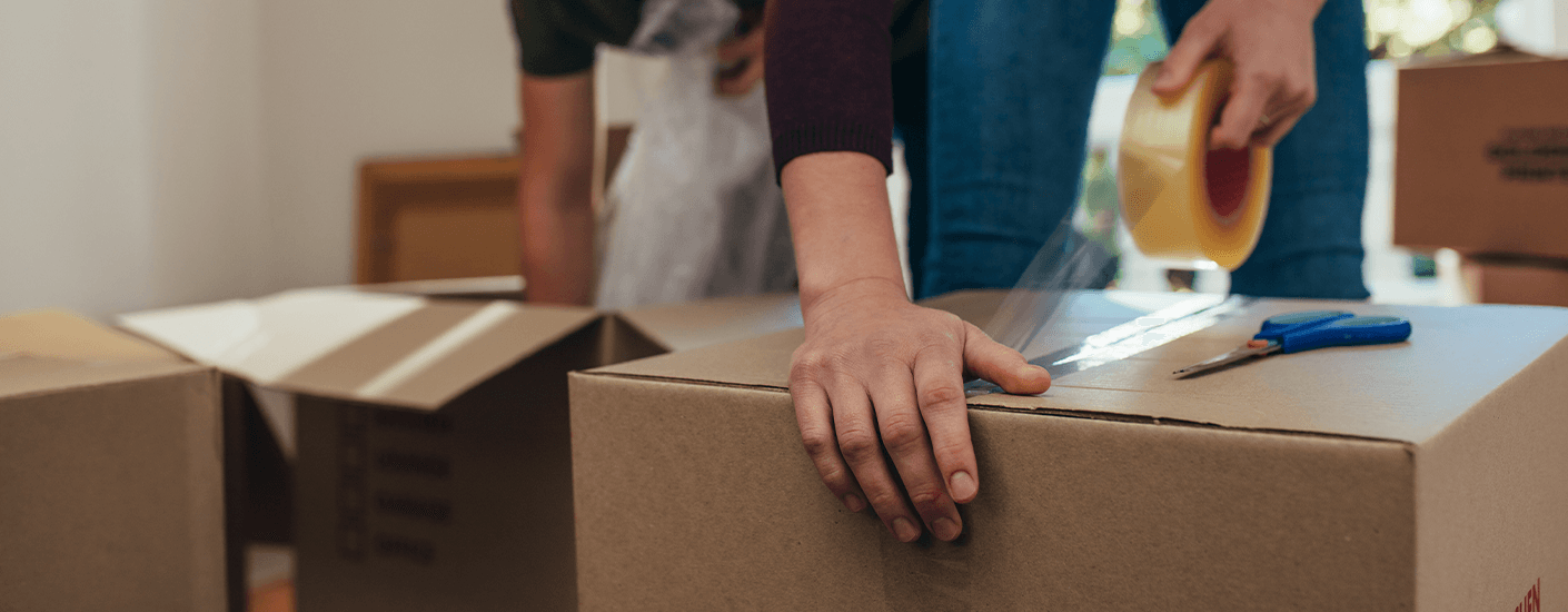 Couple packing cardboard boxes and sealing them with tape while preparing to move into a new home after closing.