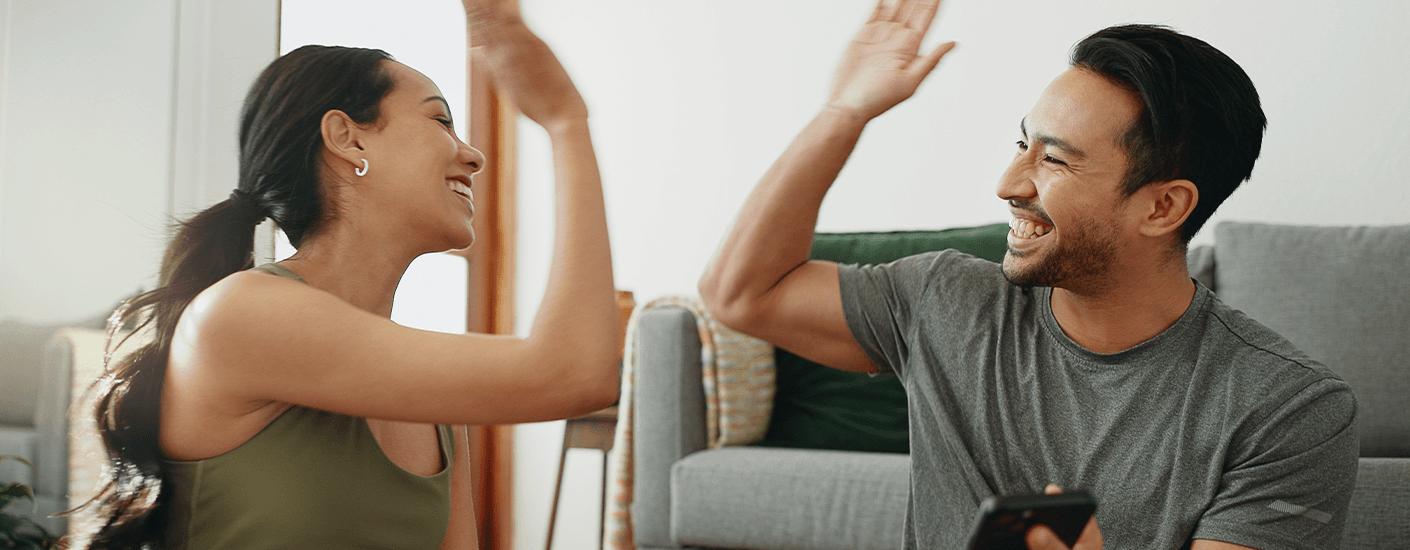 Happy couple high-fiving in their living room, representing the excitement of being cleared to close on a new home.