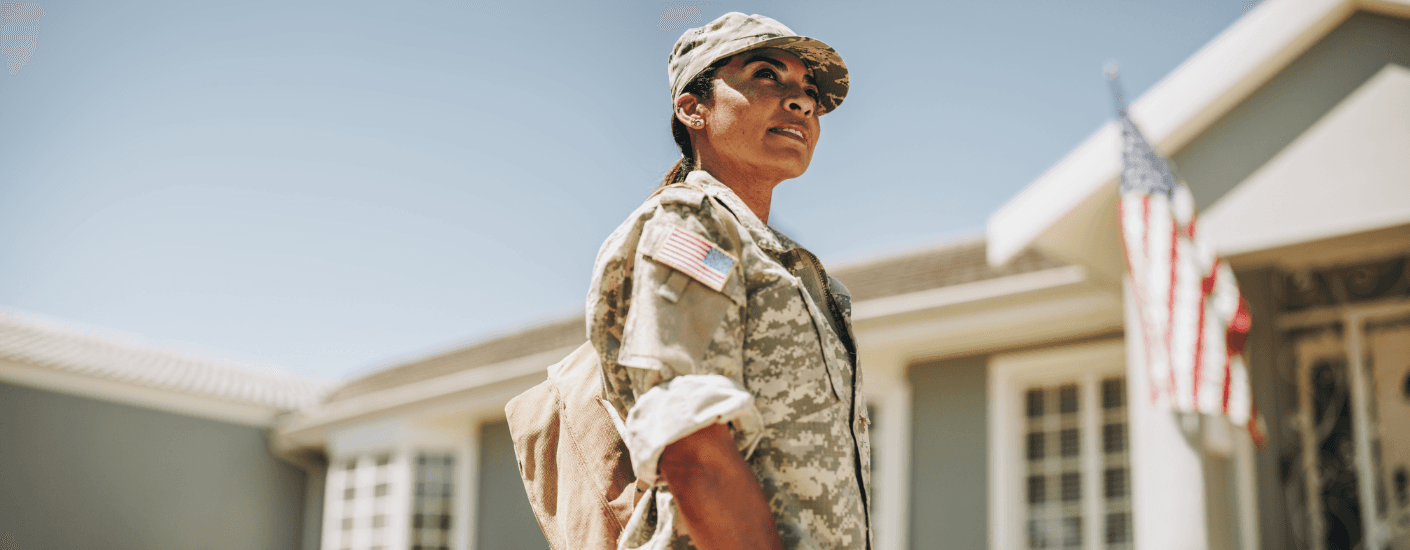 Service member in uniform outside a home with a U.S. flag, accompanying a guide to VA home loans in Guam.